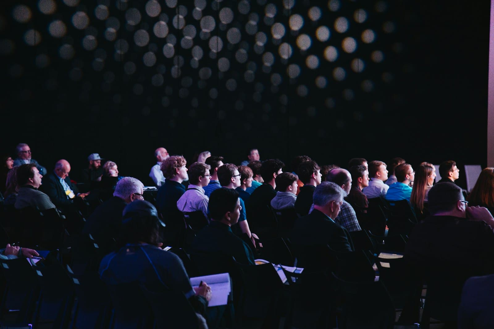 An audience in a darkened hall watching a lit stage